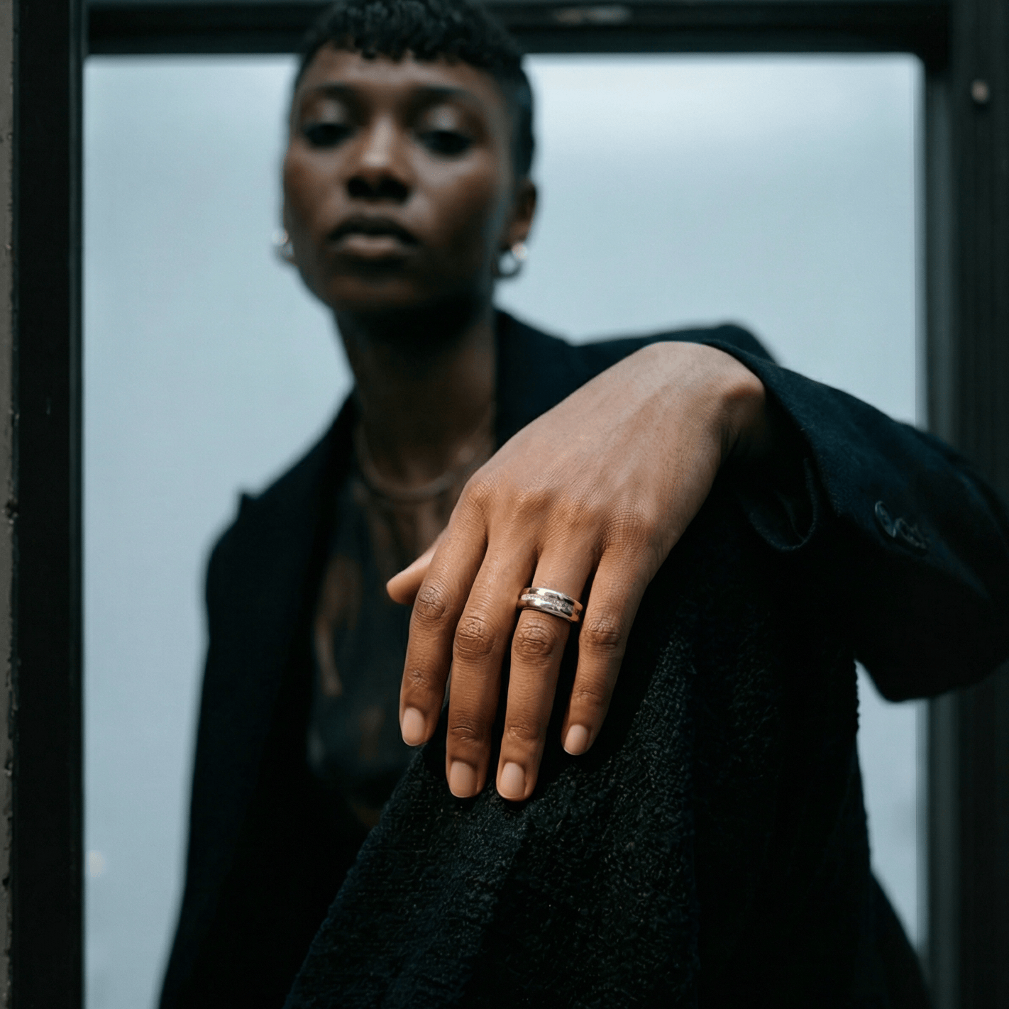 Person wearing a black coat with a hand resting on their chest, wearing a fashion smart ring.
