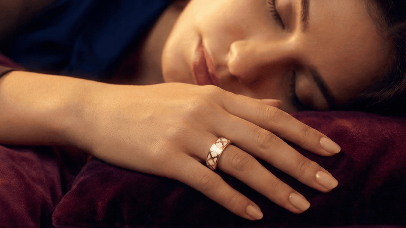 Woman sleeping with a fashionable smart ring on her finger, surrounded by soft lighting