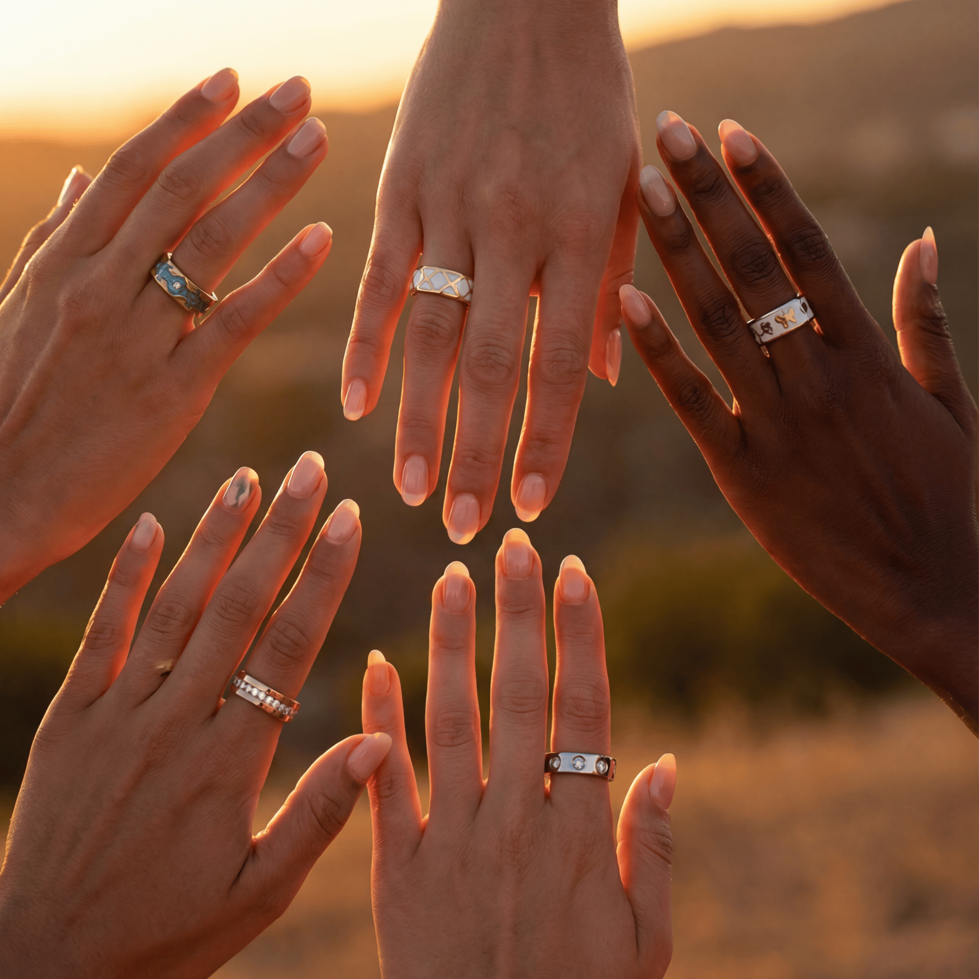 Five hands with rings held together against a sunset background