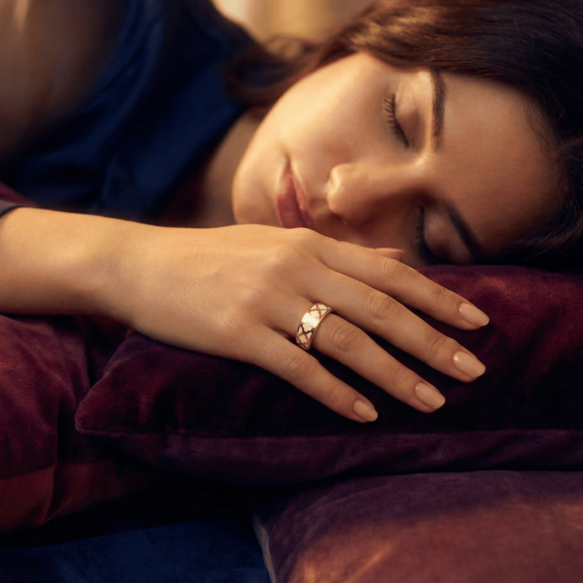 Woman sleeping with a jewellery smart ring on her finger, surrounded by soft lighting