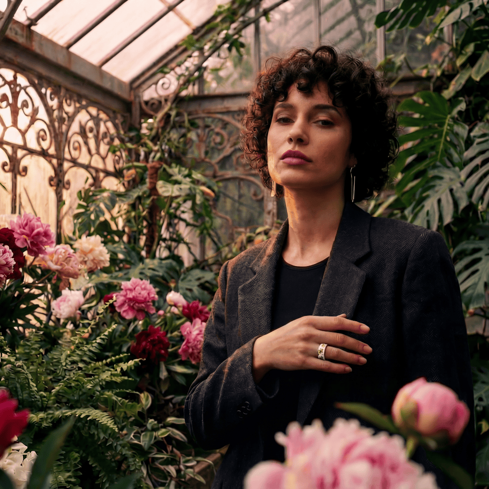 Woman wearing a fashionable smart ring standing amidst flowers in a greenhouse